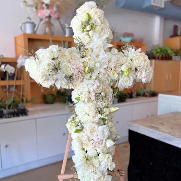 White floral cross arrangement on a wooden easel