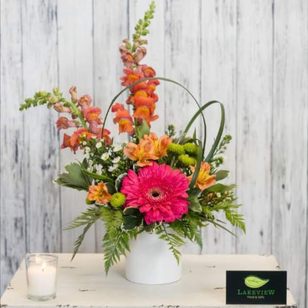 Bright mixed flower arrangement in a white vase with a candle nearby