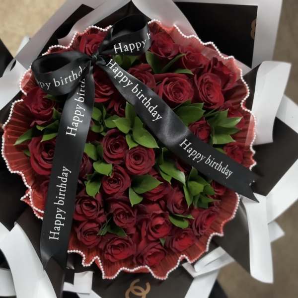Bouquet of red roses wrapped with black and white paper and birthday ribbons