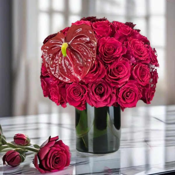 Hot pink rose arrangement in a glass vase with a red anthurium bloom
