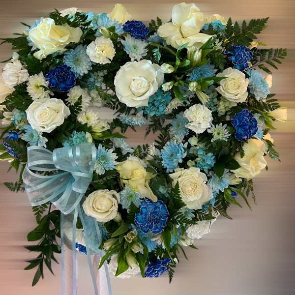 Heart-shaped wreath of white roses and blue carnations with a light blue ribbon bow