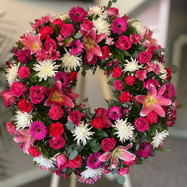 Standing wreath of pink lilies, roses, gerbera daisies and white chrysanthemums on an easel