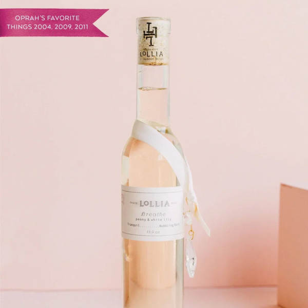 A tall clear bottle of Lollia bath oil with a ribbon tag