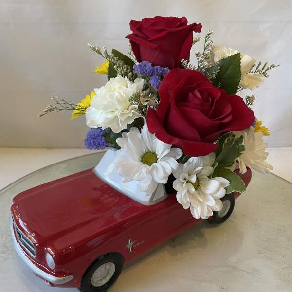 Red rose and daisy arrangement in a red toy car