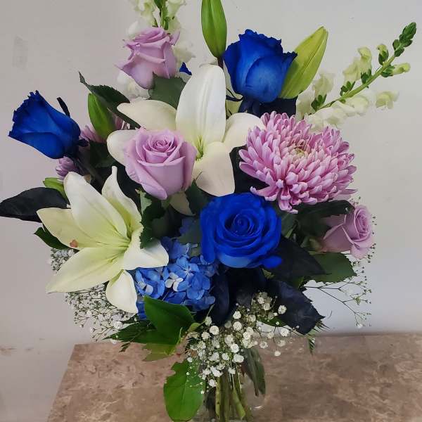 Mixed bouquet of blue and lavender roses with white lilies in a glass vase