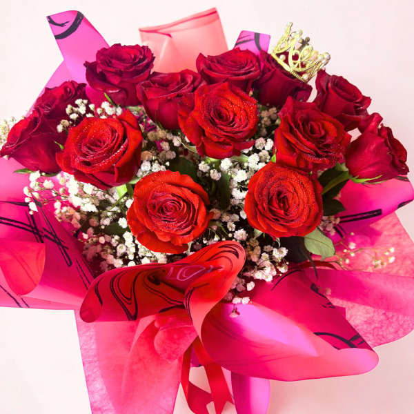 Bouquet of red roses with baby's breath and pink wrapping, topped with a small crown