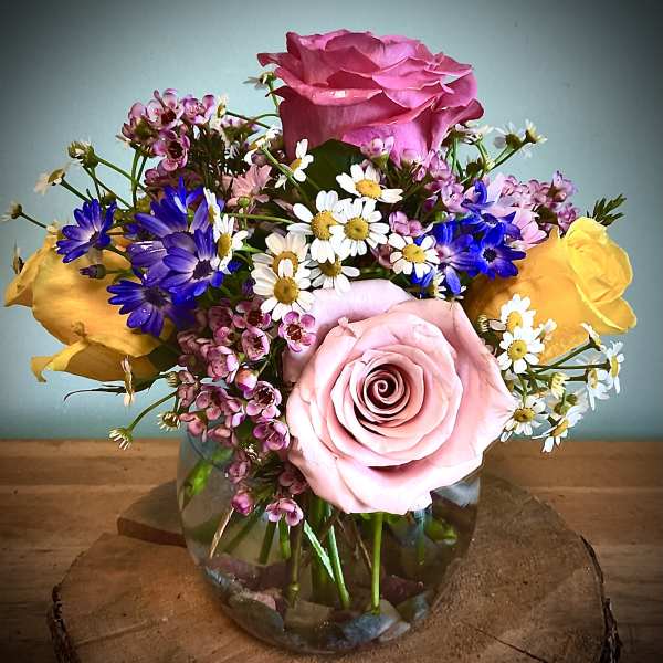 Mixed bouquet of pink and yellow roses with small daisy flowers in a glass vase