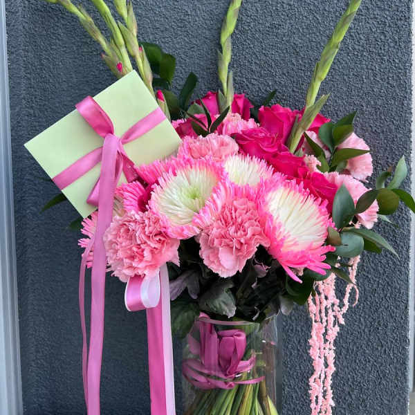 Pink bouquet with carnations, roses, and a gift card in a glass vase