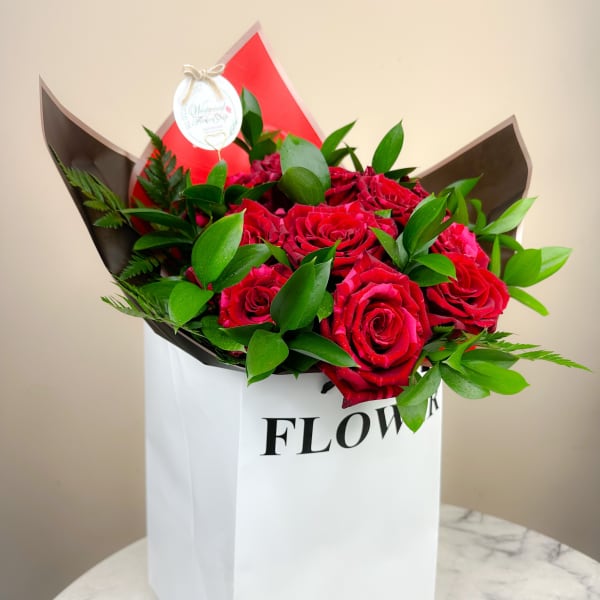 Red roses arranged in a white gift bag with green foliage