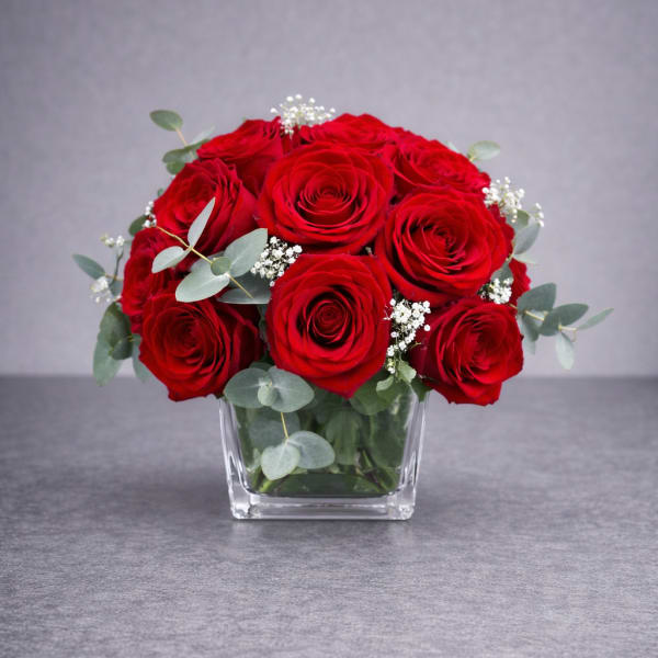 Red roses arranged in a clear square vase with eucalyptus and baby's breath