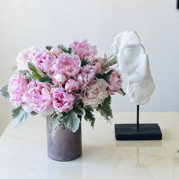 Pink peony bouquet in a purple vase beside a white sculpted bust