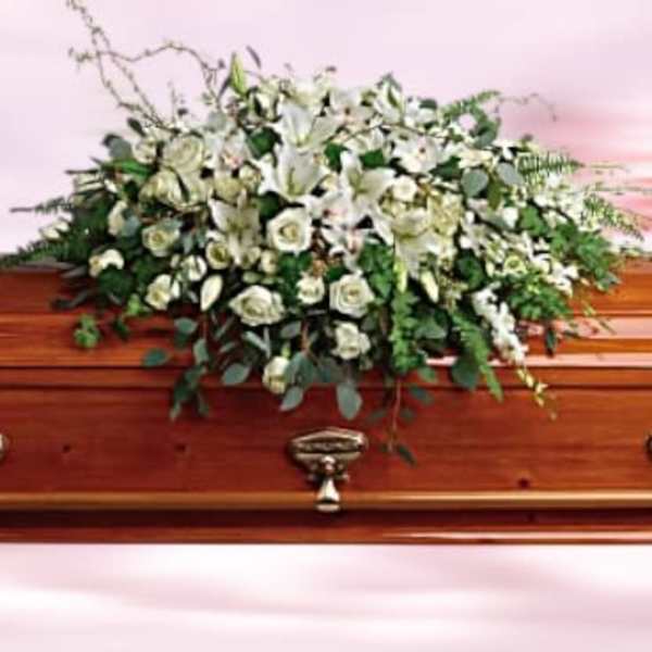 White lilies and roses arranged as a casket spray on a polished wood coffin