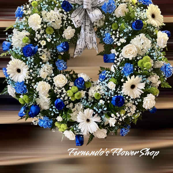 Round wreath of blue and white flowers with green accents and a printed memorial ribbon bow