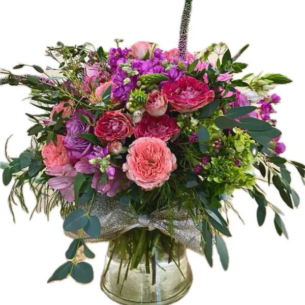 Pink and purple mixed flower arrangement in a clear glass vase with a silver ribbon bow.