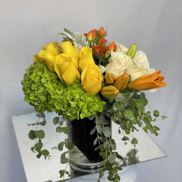 Bouquet of yellow, white, and orange roses with green hydrangea in a black vase