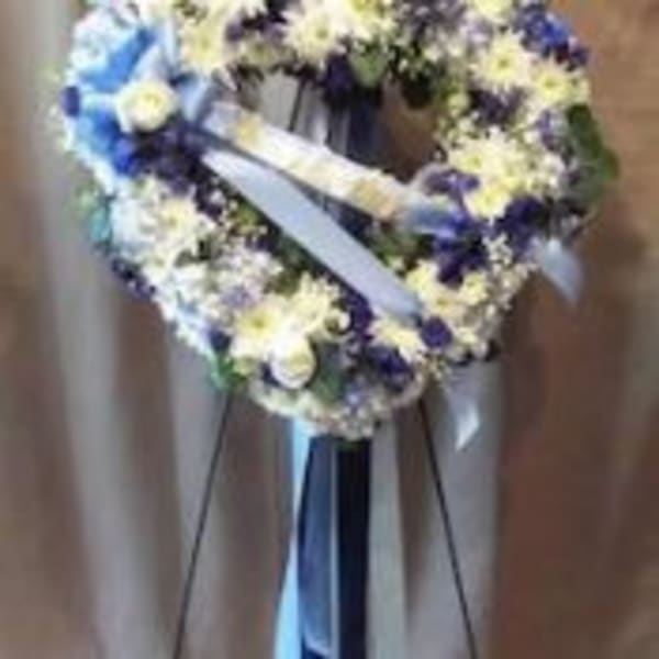 Standing round wreath of white and blue flowers with ribbons on an easel