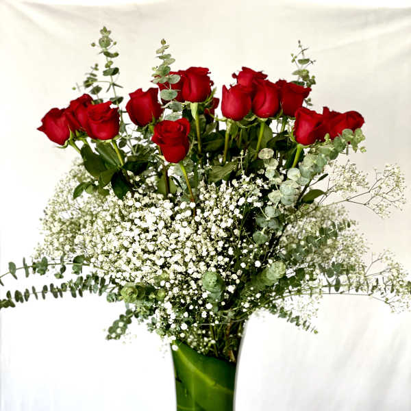Red roses in a tall glass vase with baby's breath and eucalyptus