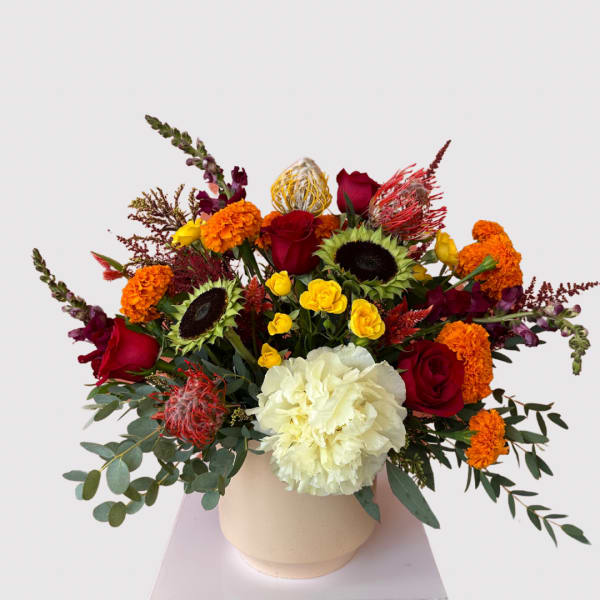 Colorful mixed bouquet in a cream vase with roses, marigolds, and sunflowers