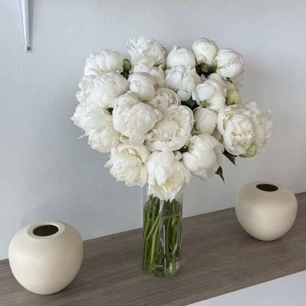 White peony bouquet in a clear glass vase on a shelf