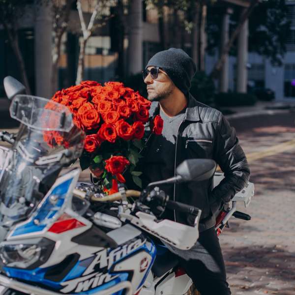 Man on a motorcycle holding a large bouquet of red roses