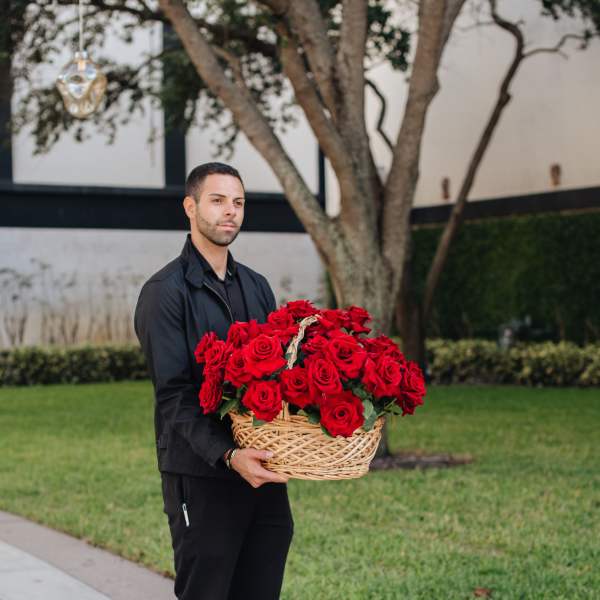 Man holding a large basket of red roses outdoors