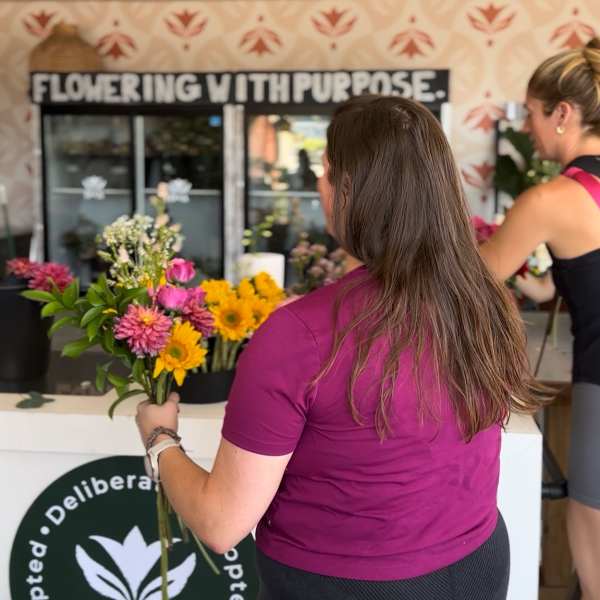 Woman holding a bouquet of pink and yellow flowers at a flower stand