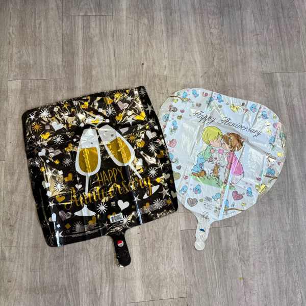 Two anniversary foil balloons lie on a wood floor.