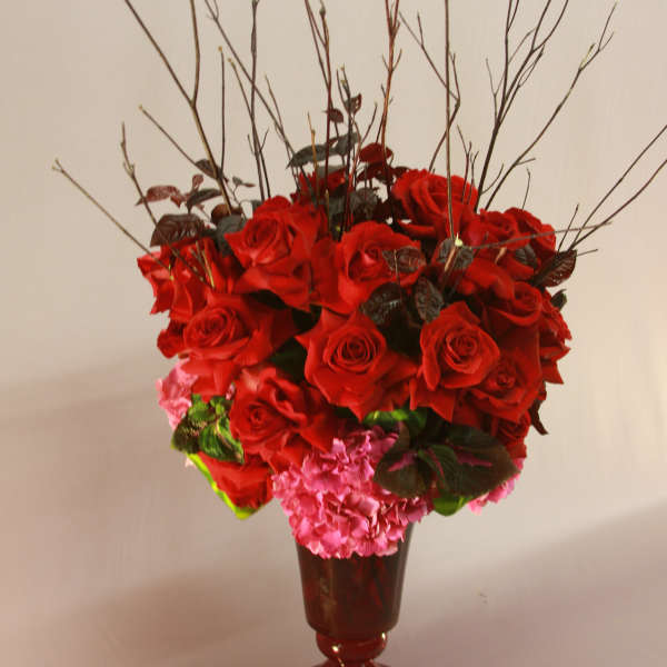 Red roses and pink hydrangeas in a red pedestal vase with tall branches
