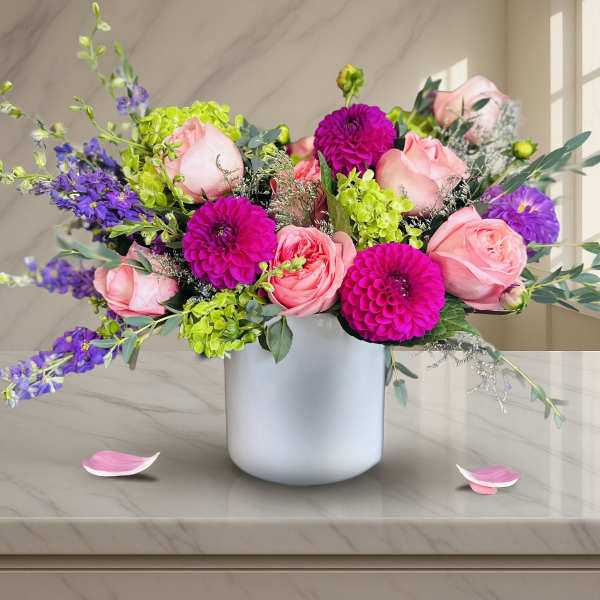 Pink roses and purple blooms arranged in a white vase