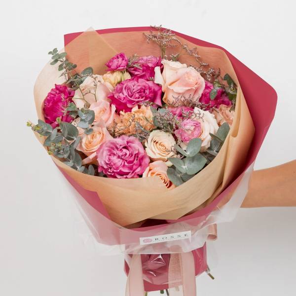 Hand-tied bouquet of pink and peach roses wrapped in tan and pink paper