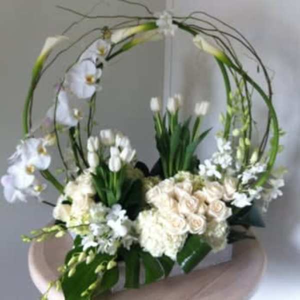 White floral arrangement with orchids and roses in a circular frame
