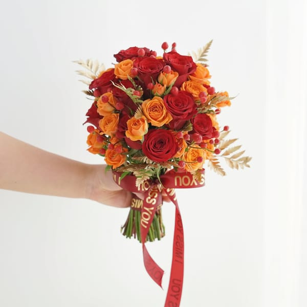 Handheld bouquet of red and orange roses with a red ribbon