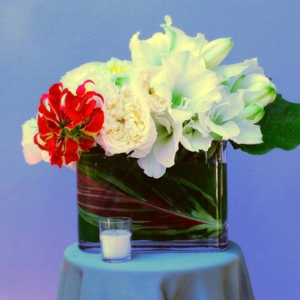 White and red flowers arranged in a square glass vase with a small candle in front