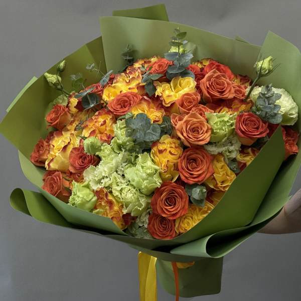 Bouquet of orange and yellow roses with green carnations wrapped in green paper