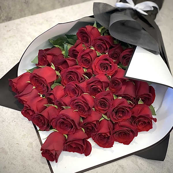 Bouquet of red roses wrapped in black paper with a white ribbon