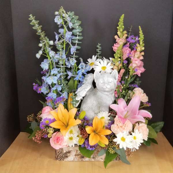 Colorful floral arrangement with a white cat figurine in a bark-covered container