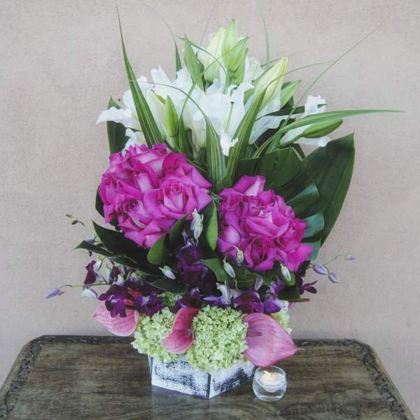 Tall floral arrangement with pink roses, white lilies, and pink calla lilies in a square vase.