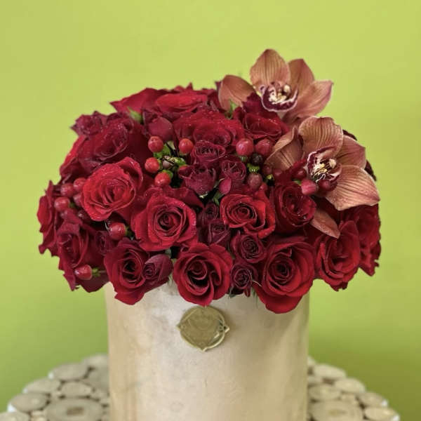 Red rose arrangement in a beige hatbox with two orchid blooms