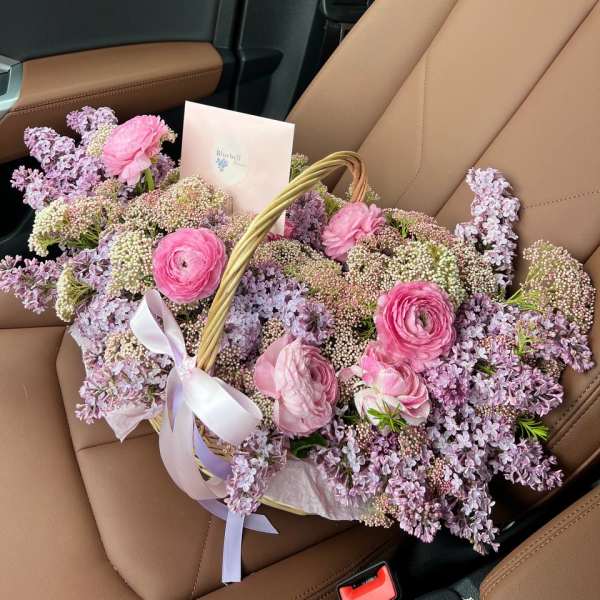 Basket of pink and lavender flowers with a ribbon on a car seat
