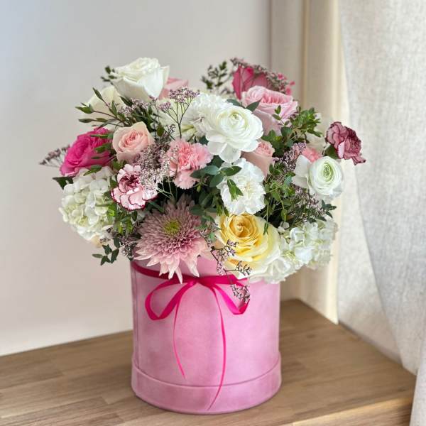 Pink hatbox arrangement with roses, hydrangeas, and a ribbon