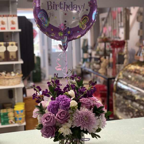 Purple flower arrangement with a Happy Birthday balloon in a glass vase