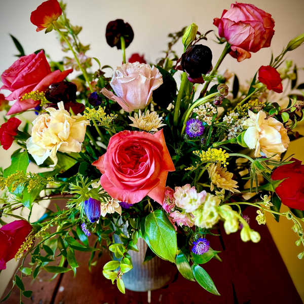 Vibrant mixed bouquet of pink and red roses with assorted blooms in a ribbed vase on a wooden table.