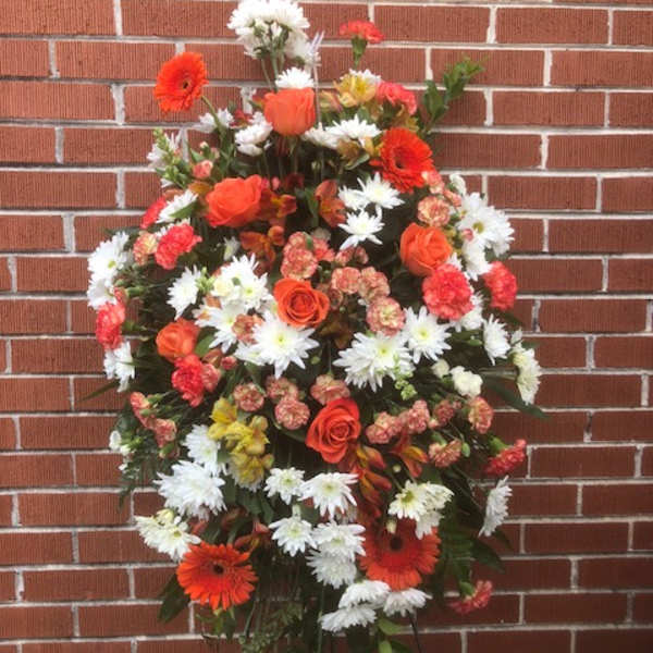 Standing floral spray with orange and white flowers on a black easel