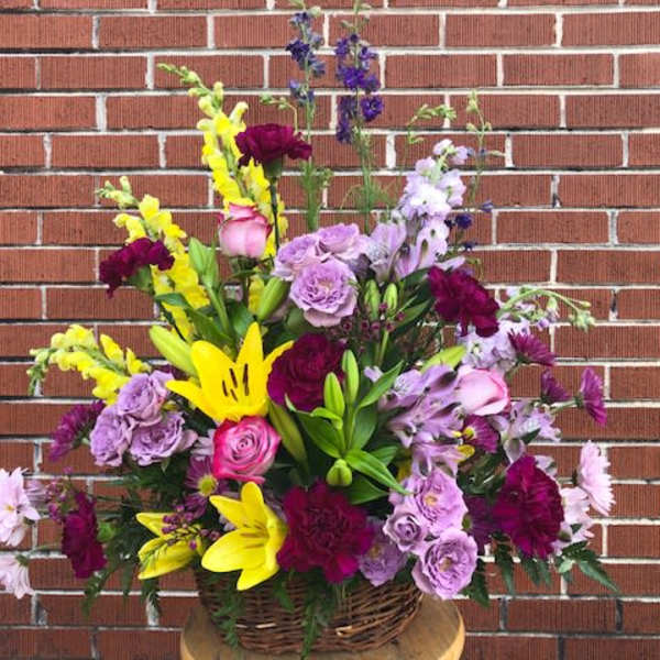 Mixed bouquet of yellow lilies, purple roses, and pink flowers in a basket