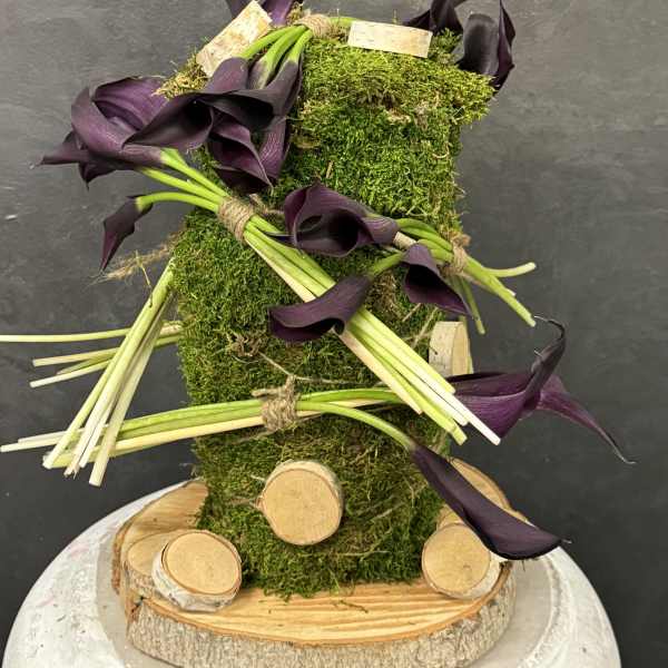 Purple calla lilies arranged on a moss-covered wooden base