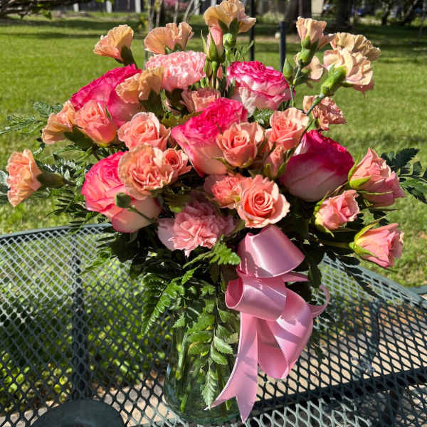 Pink and peach roses with carnations in a glass vase with a pink ribbon