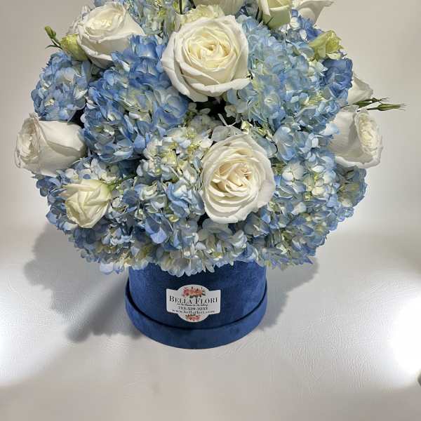 Blue hydrangeas and white roses arranged in a round velvet box