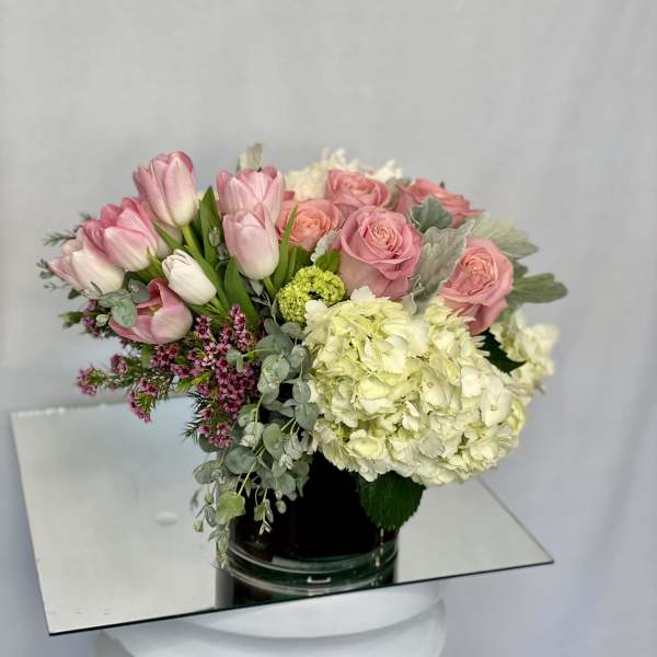 Pink tulips and roses with pale hydrangea in a glass vase