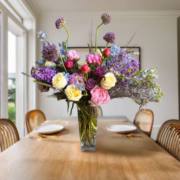 Tall mixed bouquet in a clear glass vase on a dining table