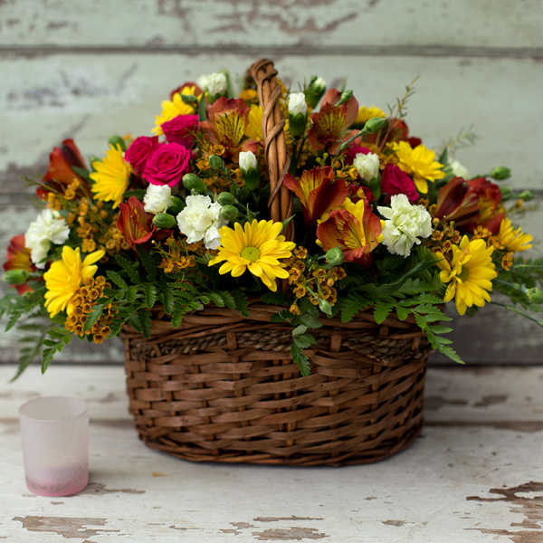 Basket of mixed flowers with yellow daisies, pink roses, and white carnations